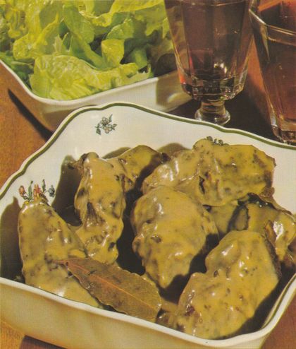 Gebratene Hasenrücken-Stücke in glänzender Sahne-Rotwein-Sauce auf einer weißen Servierplatte mit grünem Blumendekor. Im Hintergrund eine Schale mit grünem Blattsalat und ein Wasserglas auf einem Holztablett.