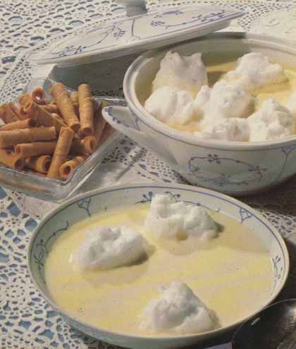 Vanillepudding mit Schneeklößchen auf einem Teller und in einer Schüssel, daneben goldbraune Waffelröllchen auf einem Glasteller. Das Geschirr mit blauem Blumenmuster steht auf einer weißen Häkeldecke.