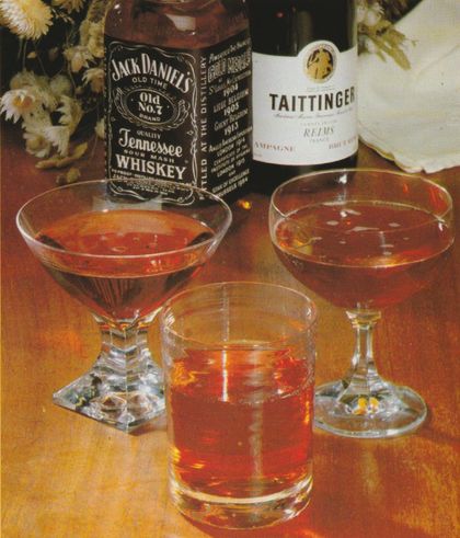 Drei Cocktails in verschiedenen Gläsern: zwei in breiten Cocktailschalen mit geometrischem Fuß und einer in einem hohen Glas mit Eiswürfeln. Im Hintergrund stehen eine Flasche Jack Daniel’s Whiskey und eine Flasche Taittinger Champagner. Hinten im Bild ein Strauß getrockneter Gänseblümchen.