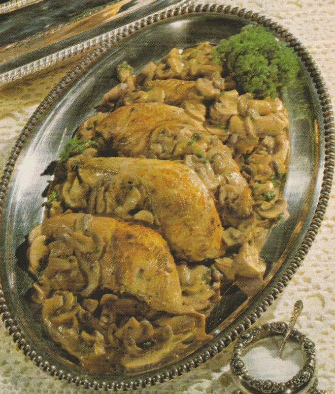 Zwei goldbraun gebratene Fasanenbrüstchen auf einem Bett aus geschmorten Champignons mit Sahnesauce, serviert auf einer ovalen Metallplatte mit gezacktem Rand. Im Hintergrund rechts ein Büschel Petersilie als Garnitur.